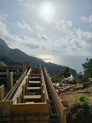 Blick auf Küstenlandschaft mit Baugerüst und Sonne über dem Meer.