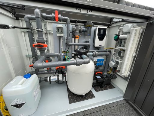 Rohrleitungsinstallation in einem technischen Raum mit Wasserbehälter und Steuerungseinheit.