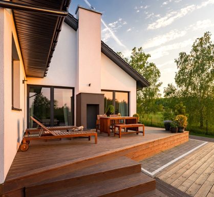 Moderne Terrasse mit Holzmöbeln und Blick ins Grüne bei Sonnenuntergang.